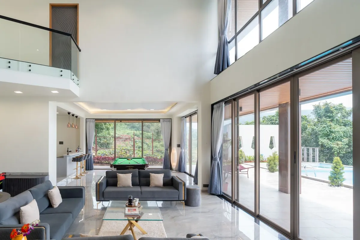 Double-height living room with a wall of full-height sliding glass doors opening to a covered terrace and pool
