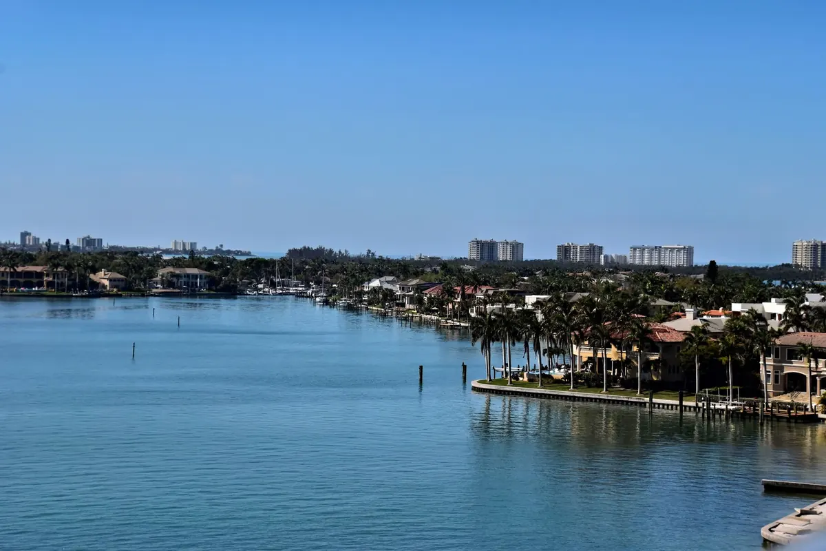 Calm blue water with palm-lined waterfront homes, docks and distant mid-rise condos