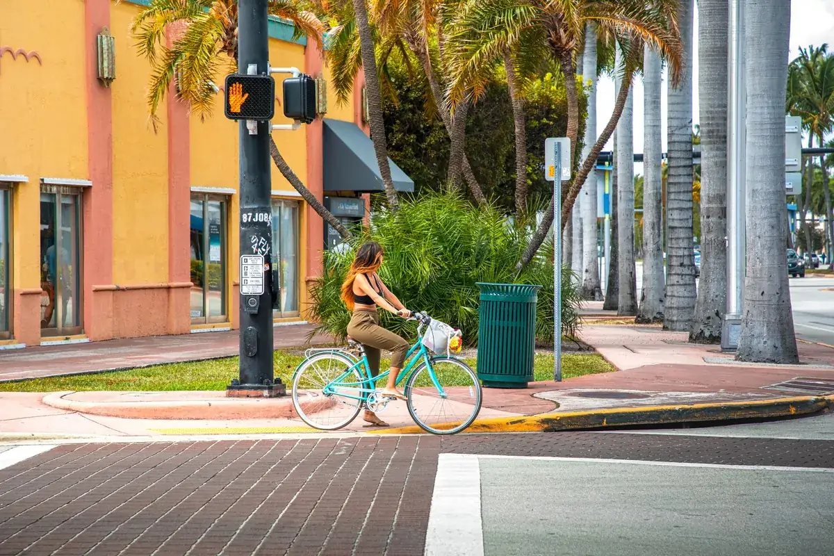 Cyclist passing a coral and yellow stucco shopfront on a palm-lined street corner