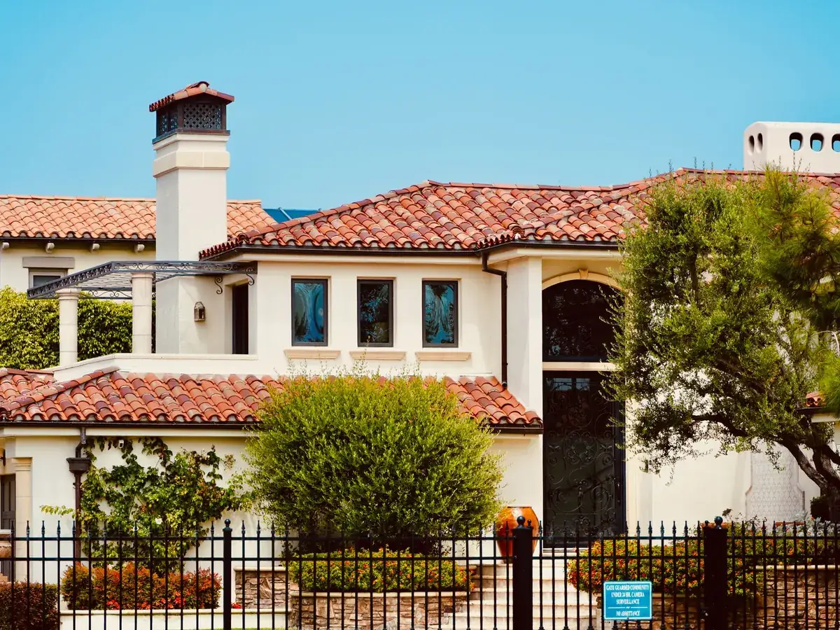 Cream stucco Mediterranean-style house with a terracotta barrel-tile roof, tall arched entry and rectangular windows behind an iron fence